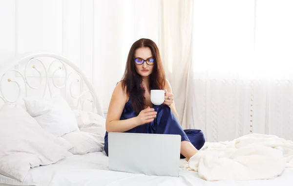 Young woman reads from tablet pc in bed, high key — Stock Photo, Image