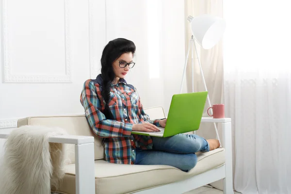 Chica joven en un sofá blanco con un ordenador portátil . — Foto de Stock