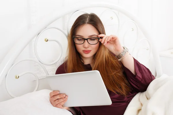 Jovem mulher lê a partir de tablet pc na cama, chave alta — Fotografia de Stock