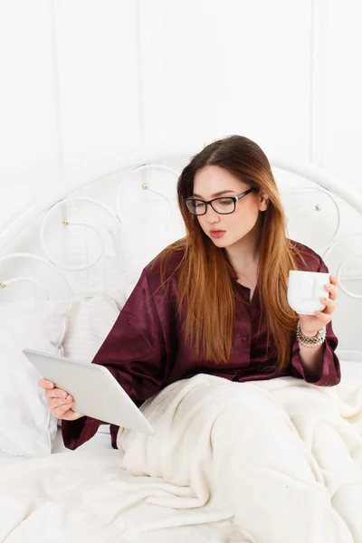 Jovem mulher lê a partir de tablet pc na cama, chave alta — Fotografia de Stock