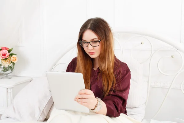 Jovem mulher lê a partir de tablet pc na cama, chave alta — Fotografia de Stock