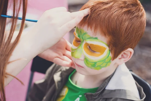 Child face painting process at redhead boy