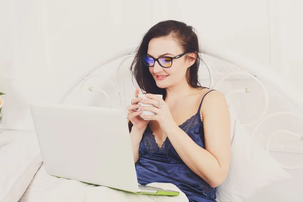 Woman reads from tablet pc in bed, high key — Stock Photo, Image