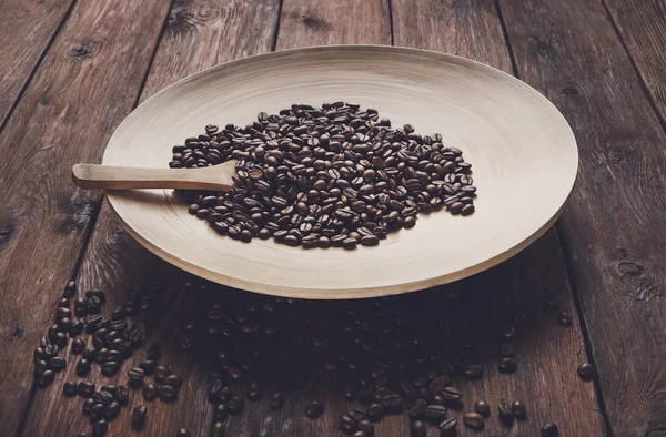 Coffee beans in bowl with wooden spoon on table — Stock Photo, Image