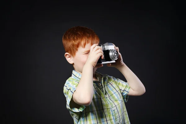 Kleiner Junge macht Foto mit Vintage-Kamera vor schwarzem Hintergrund — Stockfoto