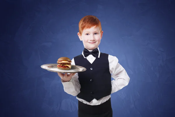 Little boy waiter stands with tray serving hamburger — Stock Photo, Image