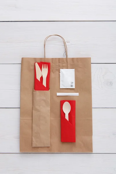 Paper bag and cutlery at white wood, food take away