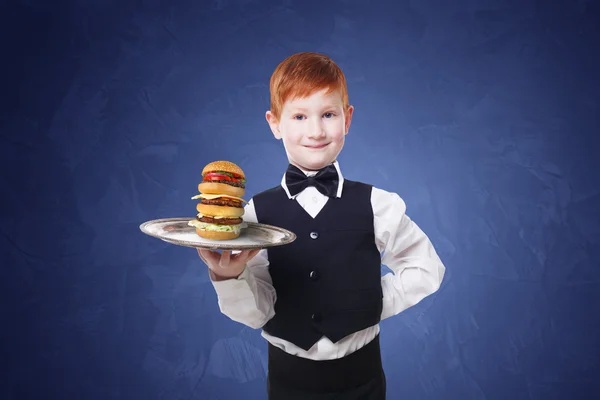 Little boy waiter stands with tray serving hamburger — Stock Photo, Image