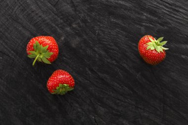 Red fresh strawberries on black rustic wood background clipart