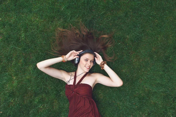 Pretty young girl listening music in earphones lying on grass — Stock Photo, Image