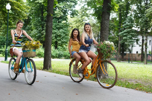 Felice boho chic ragazze cavalcare insieme su biciclette nel parco — Foto Stock