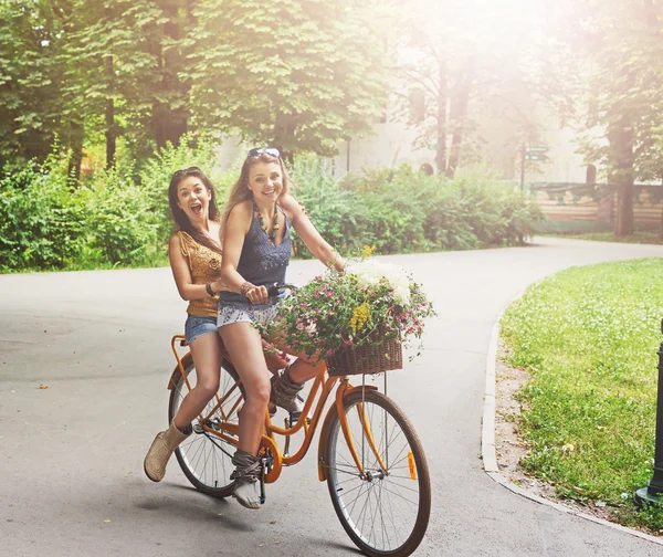 Felice boho chic ragazze cavalcare insieme su biciclette nel parco — Foto Stock