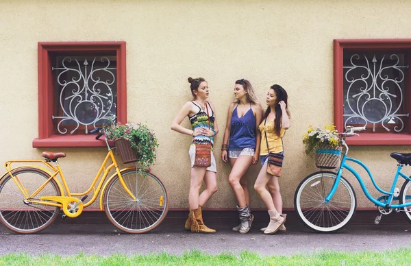 Ευτυχισμένος boho chic κορίτσια ποζάρουν με ποδήλατα κοντά σε πρόσοψη σπιτιού — Φωτογραφία Αρχείου