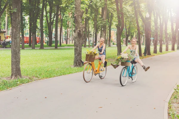 Felice boho chic ragazze cavalcare insieme su biciclette nel parco — Foto Stock