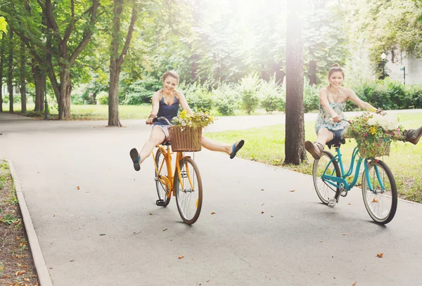 Felice boho chic ragazze cavalcare insieme su biciclette nel parco — Foto Stock