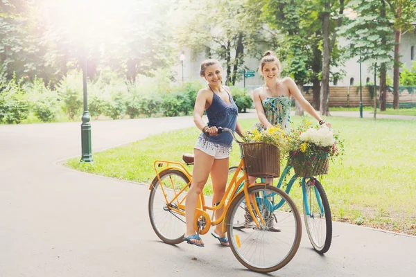 Felice boho chic ragazze cavalcare insieme su biciclette nel parco — Foto Stock