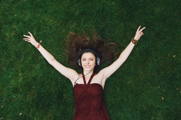 Menina bonita ouvir música em fones de ouvido deitado na grama — Fotografia de Stock