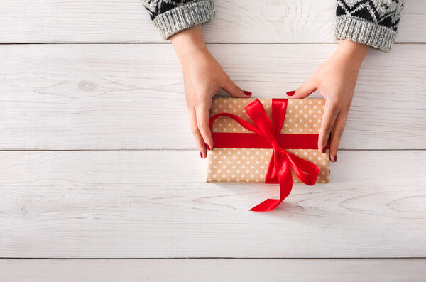 Womans hands wrapping christmas holiday present with red ribbon