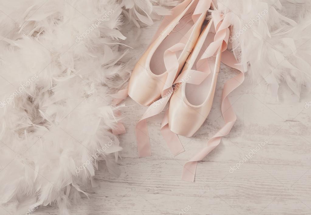 Pink ballet pointe shoes and feather on white wood