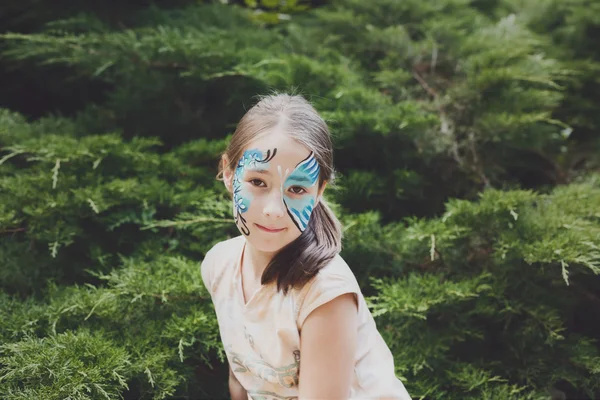 Flicka barn utomhus i parken med fjäril ansiktsmålning — Stockfoto