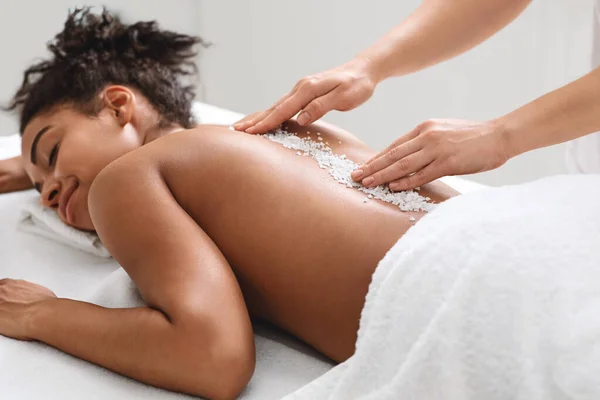 Joyful black lady getting healing salt massage at modern spa — Stock Photo, Image