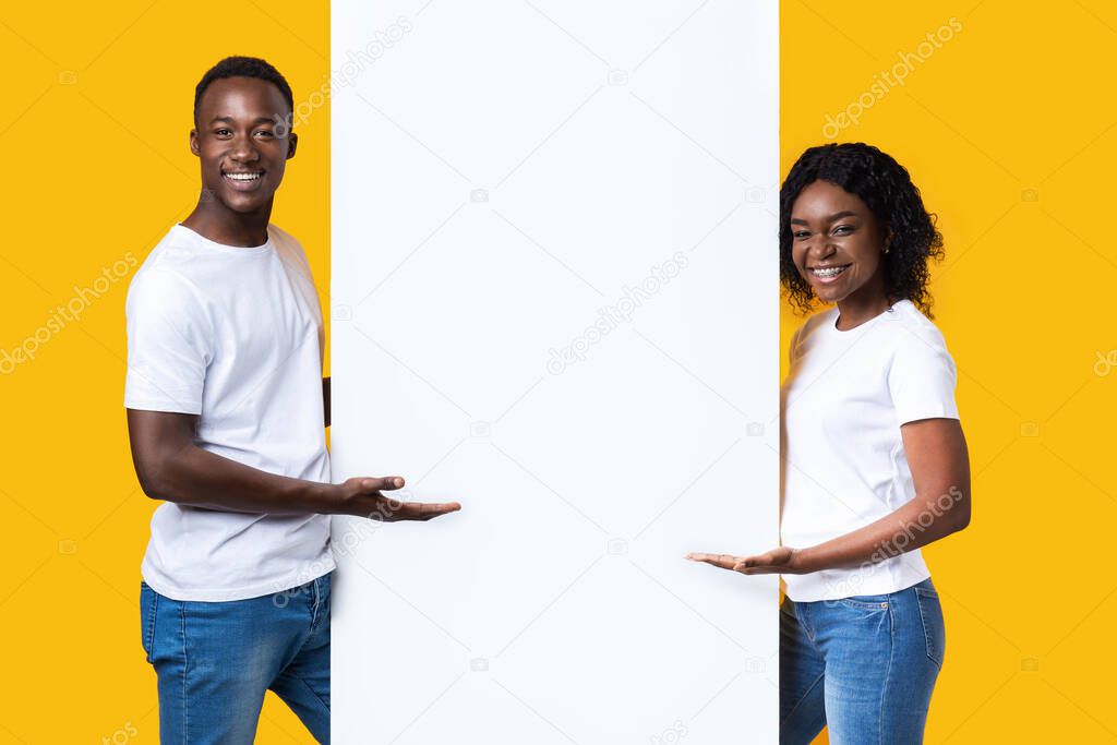 Cheerful african couple standing by empty board for advertisement