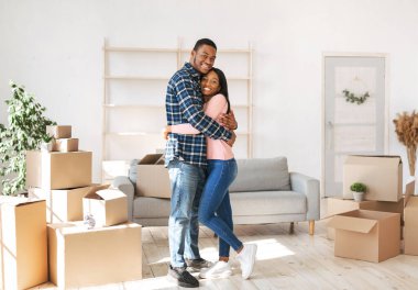 Pozitif siyah adam ve kız arkadaşı taşınma günü yeni evin oturma odasında birbirlerine sarılıyorlar.