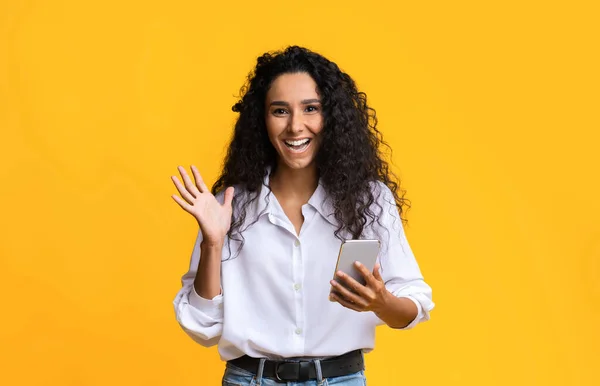 拿着智能手机站在黄色背景下的兴奋快乐的年轻女人 — 图库照片