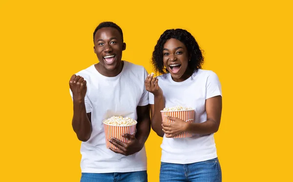 Emocionado hombre negro y mujer comiendo palomitas de maíz sobre fondo amarillo —  Fotos de Stock