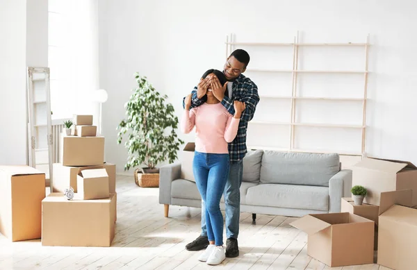 Bewegende dag concept. Millennial zwarte man sluiten zijn vriendinnen ogen in hun huis met kartonnen dozen — Stockfoto