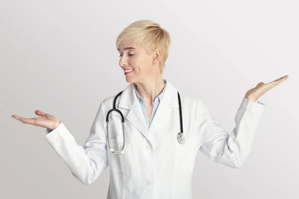 Volwassen vrouw arts in witte jas met stethoscoop steekt haar handen op voor het wegen — Stockfoto