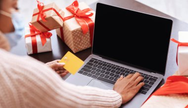 Laptop ve kredi kartı kullanan maskeli siyah bir kadın.