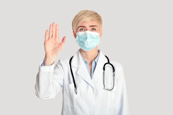 Μεσήλικη γυναίκα γιατρός σε λευκό παλτό με στηθοσκόπιο σε προστατευτική μάσκα, δείχνει στοπ με το χέρι — Φωτογραφία Αρχείου