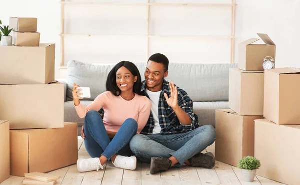 Νεαρό μαύρο ζευγάρι συνομιλεί με φίλους ή οικογένεια σε απευθείας σύνδεση στο κινητό τηλέφωνο στο νέο διαμέρισμα, πανόραμα — Φωτογραφία Αρχείου