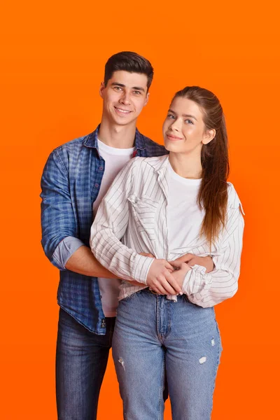 Молодой улыбающийся мужчина и женщина в повседневных и джинсовых объятиях и глядя в камеру — стоковое фото