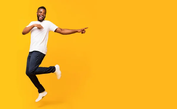 Joyful black guy jumping up and pointing aside — Stock Photo, Image