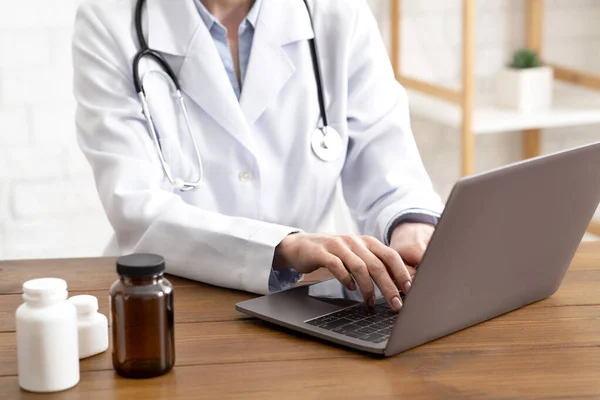 药丸、治疗和健康保护。穿着白衣、带听诊器的成年女医生在笔记本电脑上工作 — 图库照片