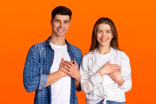 Grateful gesture concept. Pretty smiling young male and female in casual clothes keep hands on chest, being thankful — Stock Photo, Image