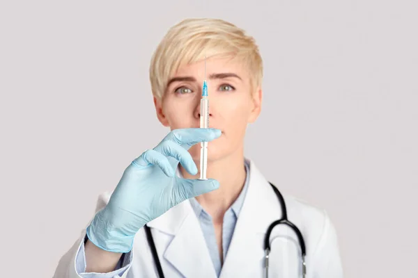 Εστίαση στη σύριγγα με φάρμακο σε λευκή επικάλυψη με στηθοσκόπιο σε λαστιχένια γάντια μεσήλικας γιατρού — Φωτογραφία Αρχείου
