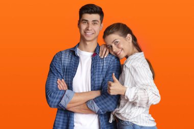 Gülümseyen adam ve kadın günlük giysiler içinde, kameraya bakın, kadın erkeğin omzuna baskı yapıyor ve başparmağını gösteriyor.