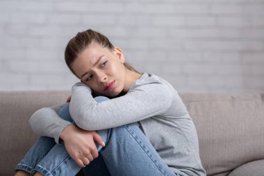 Depresyon ve endişe kavramı. Genç üzgün kadın koltukta oturuyor ve dizlerine sarılıyor, boşluğu kopyalıyor.