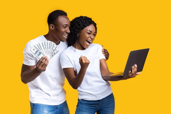 Casal negro emocional comemorando vitória com laptop e dinheiro — Fotografia de Stock