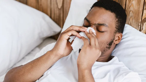 Mal hombre negro soplando la nariz en el tejido acostado en la cama — Foto de Stock