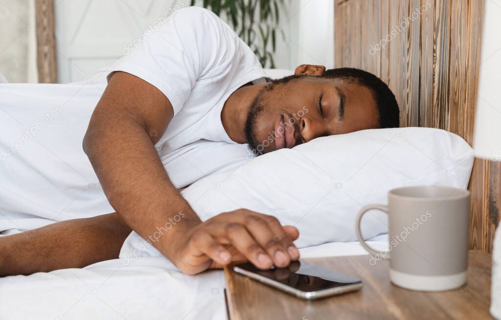 African Man Sleeping Through Alarm-Clock On Smartphone Lying In Bed