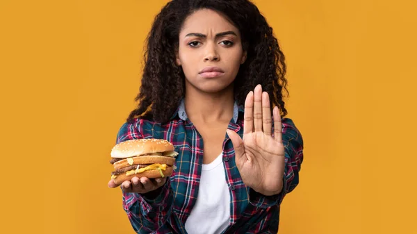 Nero donna holding hamburger e mostrando stop gesture — Foto Stock