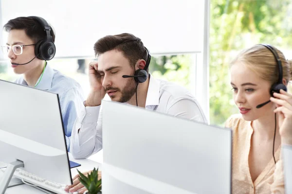 Representante del centro de llamadas cansado y sus colegas en el trabajo en la oficina de espacio abierto —  Fotos de Stock