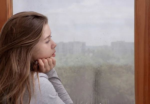 Smutna młoda kobieta wyglądająca przez okno, zagubiona w myślach, kopiująca przestrzeń. Koncepcja depresji sezonowej — Zdjęcie stockowe