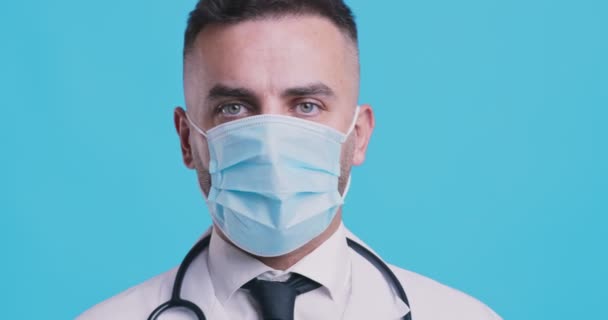 Studio portret van een serieuze arts in beschermende masker schuddende hoofd als afwijzing en ontkenning symbool, blauwe studio achtergrond — Stockvideo