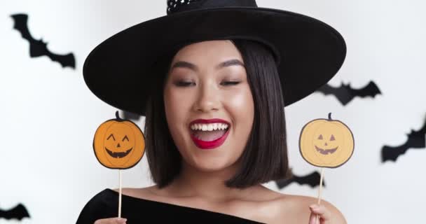 Fiesta de Halloween. Joven asiática bruja posando con calabaza foto accesorios, primer plano retrato — Vídeos de Stock