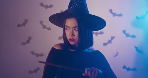 Mujer asiática seria bruja conjurando con varita mágica en luces de neón. Halloween concepto de misterio — Vídeos de Stock